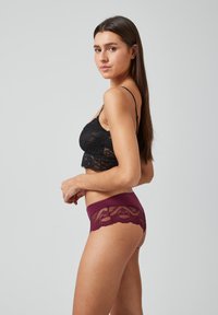 Zwarte kanten bralette met dunne bandjes, gecombineerd met burgundy boyshorts met kanten accenten, met gebogen randen en semi-doorschijnende textuur.