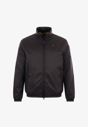 Giacca nera con zip e colletto alla coreana, tasche laterali con zip e piccola toppa nera sul petto sinistro e sulla manica.