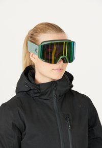 Des lunettes de ski avec une monture verte, un large verre teinté affichant des rayures arc-en-ciel, et une sangle douce et ajustable, portées avec une veste noire.