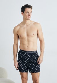 Čierne bavlnené boxerky s bielym vzorom stylizovaných písmen, s elastickým pásom označeným "KARL LAGERFELD." Štandardný strih.