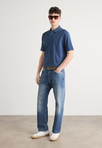 Ναυτικό πόλο μπλουζάκι, ανοιχτό μπλε τζιν και λευκά αθλητικά παπούτσια με μπεζ λεπτομέρειες. Γυαλιά ηλίου και καφέ ζώνη ολοκληρώνουν το σύνολο.