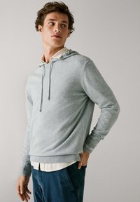 Lichtgrijze hoodie met trekkoord, gebreide textuur en contrasterende geribbelde manchetten. Draag over een witte kraagshirt en gecombineerd met blauwe broek.
