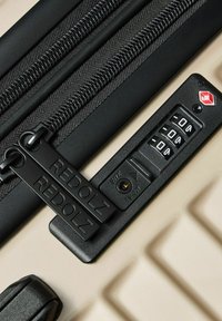 Valise beige avec poignées à double zipper noir étiquetées "REDOLZ" et un cadenas TSA à combinaison à trois chiffres intégré.