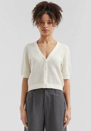 Ivory gebreide cardigan met een ruitpatroon, korte pofmouwen, v-hals en knopen aan de voorkant; gecombineerd met grijze wijde broek.