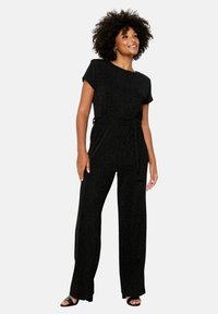 Melna, spīdīga kombinezona ar īsām piedurknēm, platām kājām un savilktu jostu. Gluda tekstūra un smalka spīdība. Vienkāršs, elegants dizains.