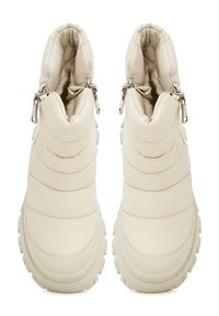 Bottines couleur crème avec texture matelassée, dotées de fermetures éclair sur les côtés et de semelles robustes pour une meilleure adhérence. Doublure douce visible à l'intérieur.