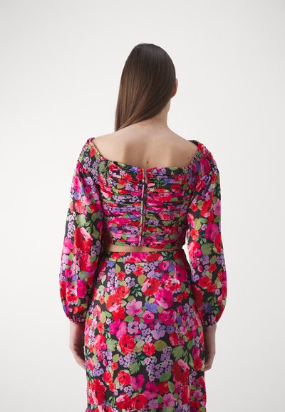 Set coordinato floreale con top arricciato e maniche a sbuffo, caratterizzato da motivi vibranti di rosa, rosso e verde su tessuto leggero. Chiusura con zip sul retro visibile.