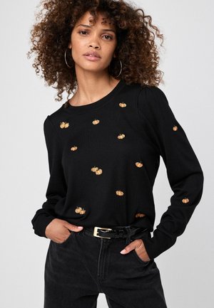 Black sweater with long sleeves, featuring gold and orange pumpkin embroidery. Ribbed cuffs and hem; worn with dark jeans and a black belt.