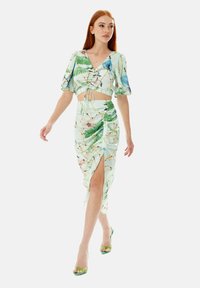 Two-piece outfit featuring a cropped top and high-slit skirt. Light green fabric with tropical floral print. Short, puffed sleeves present.