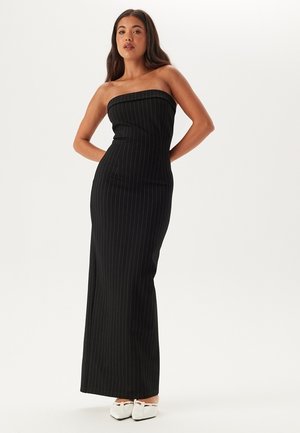 Robe maxi noire sans bretelles avec des rayures verticales. Conçue avec un corsage ajusté et une longue jupe fluide. Tissu lisse et détails minimes.