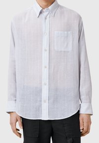 Vaaleansininen, pitkähihainen napillinen paita tekstuurikankaasta. Ominaisuuksiin kuuluu yksi rintatasku ja hienovaraiset pystysuorat raidat. Napilliset hihansuut.