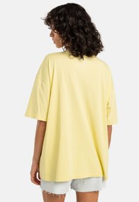 Gul oversized T-shirt i blødt materiale med korte ærmer og rund hals, parret med lyseblå denimshorts.