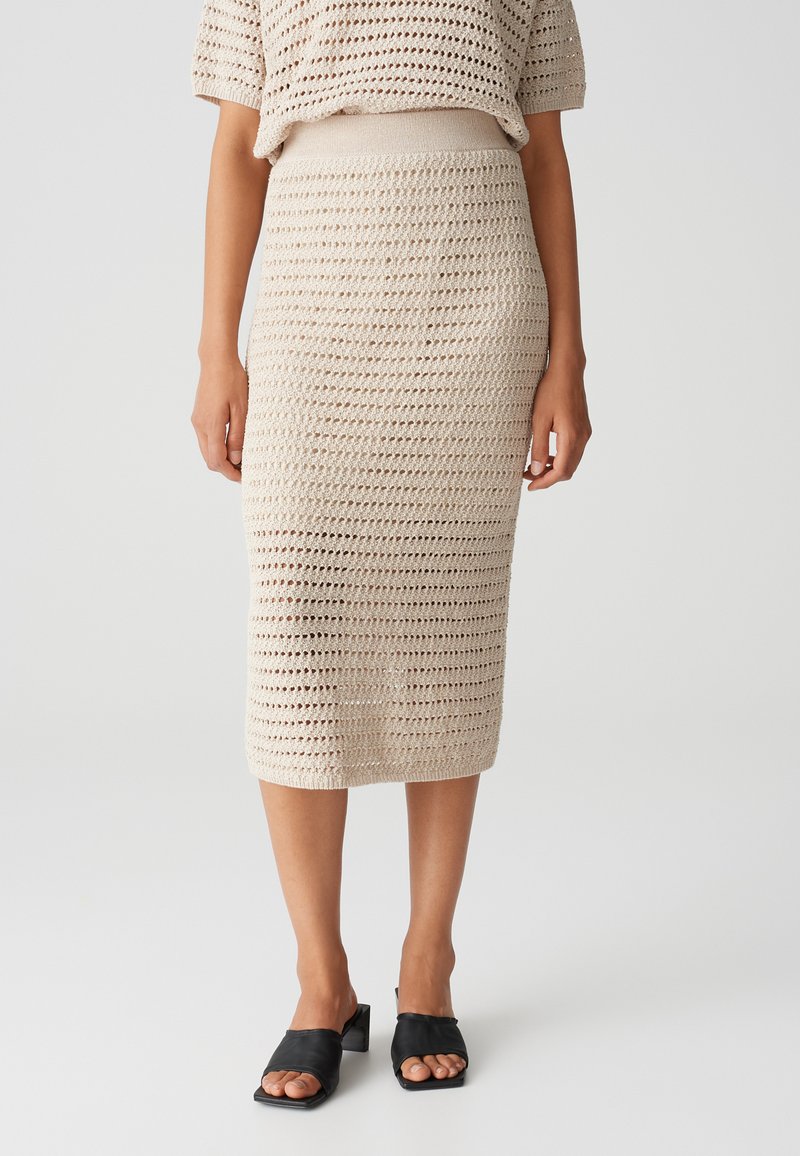 Beige Midikleid mit offener Webstruktur, elastischem Bund und glatter Textur, kombiniert mit schwarzen offenen Mules.