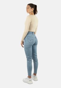 Beige langärmeliges, cropped Oberteil, kombiniert mit hochgeschnittenen hellblauen Jeans. Fußbekleidung: weiße Sneaker. Die Rückansicht zeigt das schmale Design der Jeans und die Taschen.