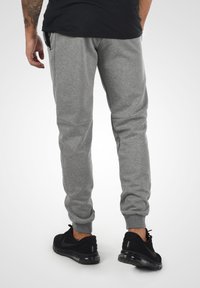 Grå sweatpants med elastiske manchetter, med sidelommer og en glat tekstur. Sammen med sorte træningssko for kontrast.