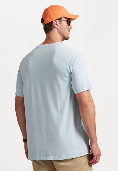 Gaiši zils īso piedurkņu T-krekls ar brīvu piegriezumu, mīkstu tekstūru, apaļu kakla izgriezumu un taisnu apakšmalu, valkāts ar khaki biksēm.