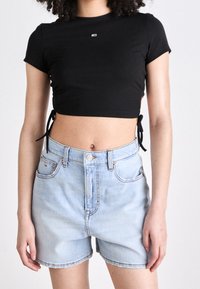 Czarny prążkowany crop top z krótkimi rękawami i związaniami po bokach, w połączeniu z jasnoniebieskimi szortami dżinsowymi o wysokim stanie z zapięciem na guziki z przodu.