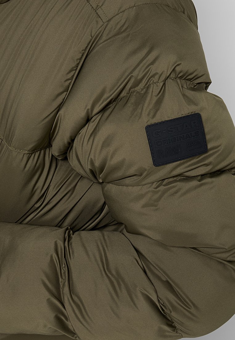 Olivegrüner gepolsterter Jacke mit strukturierter Oberfläche, ausgestattet mit einem schwarzen Gummilogo-Patch am Ärmel und elastischen Bündchen für eine gute Passform.