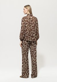 Leopardenmuster, Seidenbluse mit Puffärmeln, kombiniert mit passenden weit geschnittenen Hosen. Die Farben umfassen Beige, Braun und Hellgrau.