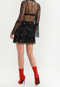 Schwarzes Kleid mit Blumenstickerei, transparenten langen Ärmeln und einem mehrlagigen Rock. Kombiniert mit roten High-Heel-Stiefeln und passenden Socken.