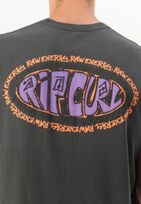 Fekete pamut póló, amelyen egy nagy, ovalis grafika látható lila és narancssárga színben, a "RIP CURL" és "RAW ENERG" feliratokkal körülötte.