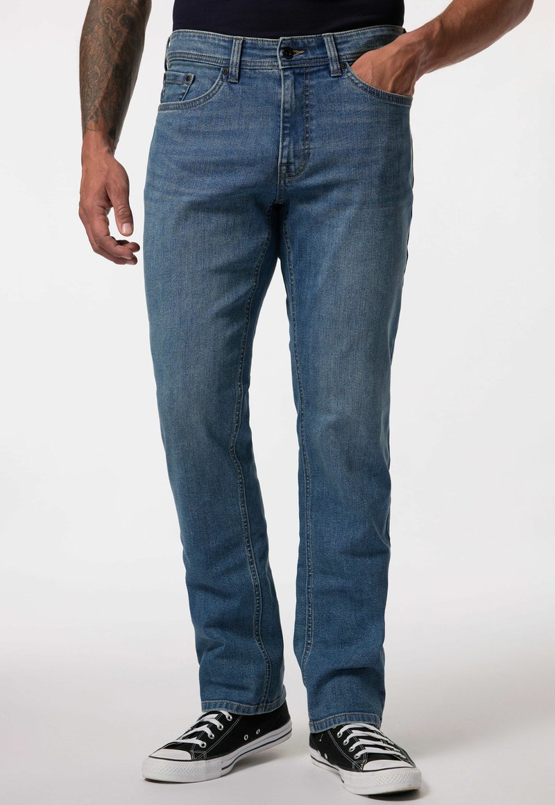 Jeans de mezclilla azul con corte recto, diseño de cinco bolsillos, acabado desgastado y cierre de botón metálico. Usados con zapatillas negras.