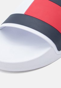 Σανδάλι slide με λευκή σόλα και επιφάνεια με υφή. Το πάνω μέρος έχει κόκκινες, μπλε και λευκές ρίγες από λείο υλικό που μοιάζει με καουτσούκ.