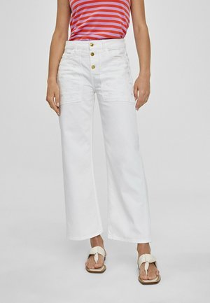Personne portant un pantalon blanc à jambes larges avec trois boutons dorés et des poches avant, associé à un haut sans manches rayé rouge et rose et des sandales blanches.