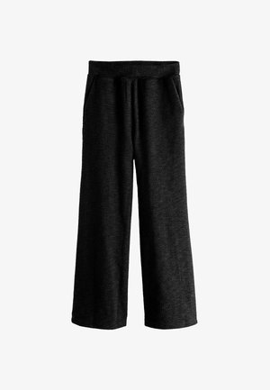 Costum texturat negru, format dintr-o bluză lejeră și pantaloni. Țesătura este moale, cu un pachet vizibil, completată de o brățară din lanț de aur.