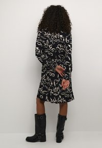 Rochie bleumarin cu un model floral alb, mâneci lungi și o croială lejeră, asociată cu cizme negre până la genunchi cu accente cu catarame.