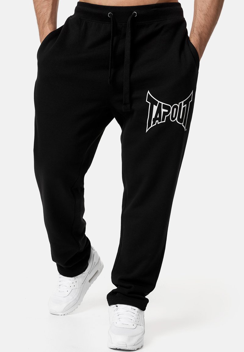 Black jogger pants made of soft material, featuring a white "TAPOUT" logo on the left leg, with an elastic waistband and drawstring.
