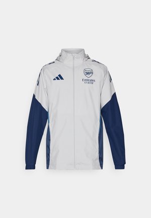 Witte sportjack met marineblauwe accenten, voorzien van een volledige rits, capuchon en logodetails. Gemaakt van lichtgewicht, waterafstotend materiaal.