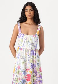 Robe d'été florale en tissu léger avec un décolleté carré, de larges bretelles et une taille froncée, ornée de motifs de fleurs colorées.