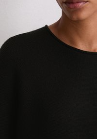 Schwarzer Strickpullover mit rundem Halsausschnitt, strukturiertem Stoff und lockerer Passform, mit sichtbaren Nähten entlang des Kragens.