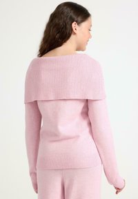 Rosa Pullover mit geripptem, schulterfreiem Halsausschnitt und langen Ärmeln, aus einem weichen Material mit glatter Textur gefertigt.