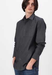 Long-sleeve dark gray button-up shirt with subtle stripes, collar, and a pocket on the left chest. Made of smooth fabric, relaxed fit.