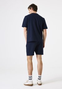 Marineblauwe katoenen t-shirt en bijpassende shorts, met een relaxte pasvorm en een zachte textuur. Witte sneakers met zwart-geaccentueerde sokken maken de look af.