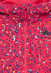 Heldere rode jas met een luipaardprintpatroon in paars, geel en blauw. Voorzien van een ritssluiting aan de voorkant en een zwart berglogo aan de zijkant.