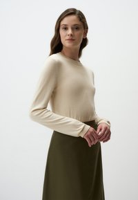 Maglione beige a maniche lunghe con scollatura rotonda, abbinato a una gonna verde scuro. Texture morbida e silhouette aderente. Design minimalista.