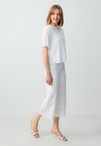 Wit, geborduurd twee-delig outfit met een top met korte mouwen en wijde broek. Het ajourontwerp heeft decoratieve uitsparingen en gegolfde randen.