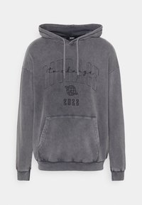 Sudadera gris con bolsillo frontal, cordones y un diseño impreso que incluye la palabra "CORAJE" y el año "2022."