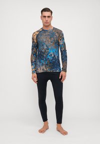 Tricou sport cu mânecă lungă într-un model multicolor de blue și maro, cu tehnica tie-dye, asociat cu colanți negri ajustați. Ambele sunt fabricate dintr-un material elastic.