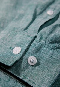 Groene stoffen textuur met zichtbare stiksels en twee witte knopen. Het ontwerp is casual en heeft een flap die over het knoopgedeelte valt.