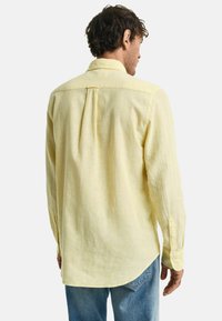 Lichtgele button-up shirt met een rugplooidetail, voorzien van lange mouwen en een licht gebogen zoom. Gemaakt van een zachte, gestructureerde stof.