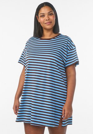 Kvinde med skulderlangt sort hår iført en kortærmet blå og brun kjole med vandrette striber og sideslids, der smiler let.