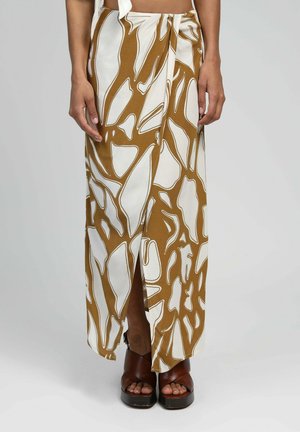 Jupe maxi avec un motif abstrait marron et blanc, dotée d'une fente sur le côté et d'un tissu léger. Associée à des sandales à plateforme marron.