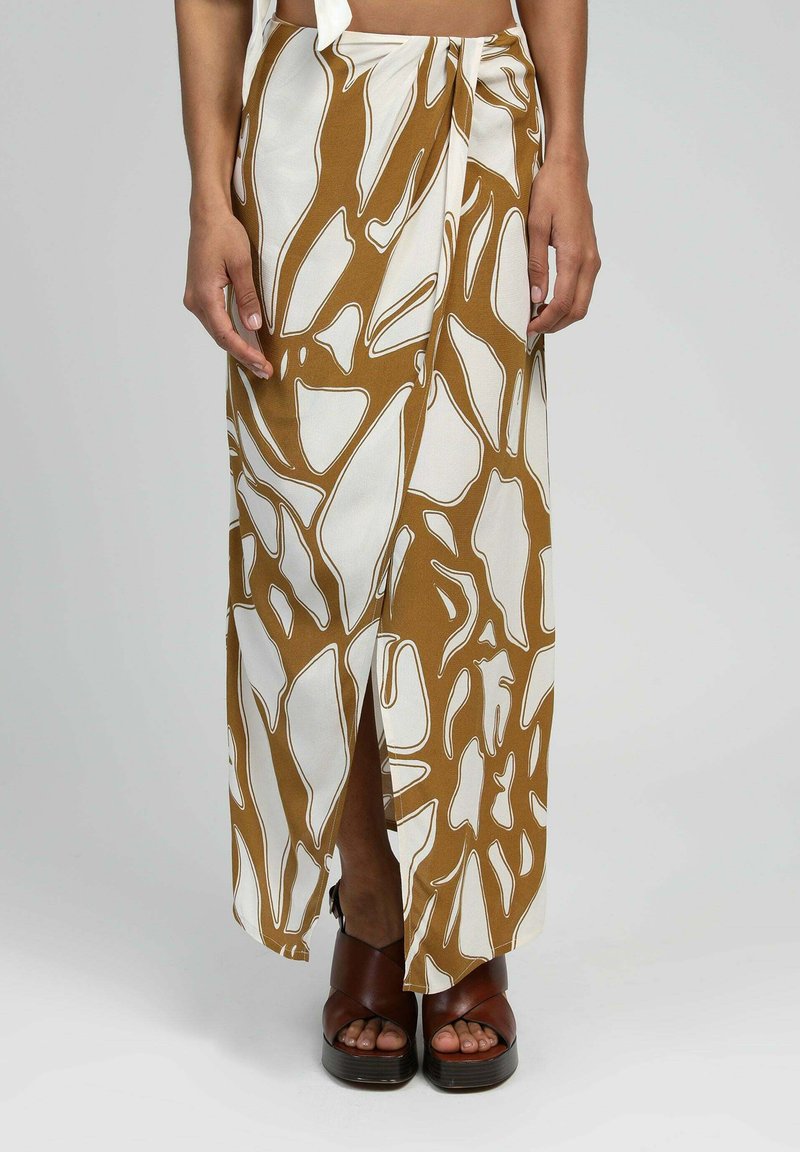 Jupe maxi avec un motif abstrait marron et blanc, dotée d'une fente sur le côté et d'un tissu léger. Associée à des sandales à plateforme marron.