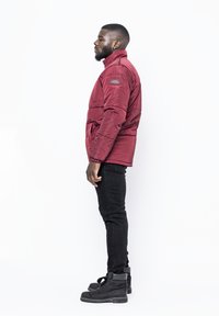 Giacca a puffo rossa con colletto alto e dettagli cuciti, abbinata a jeans skinny neri e stivali neri con lacci.