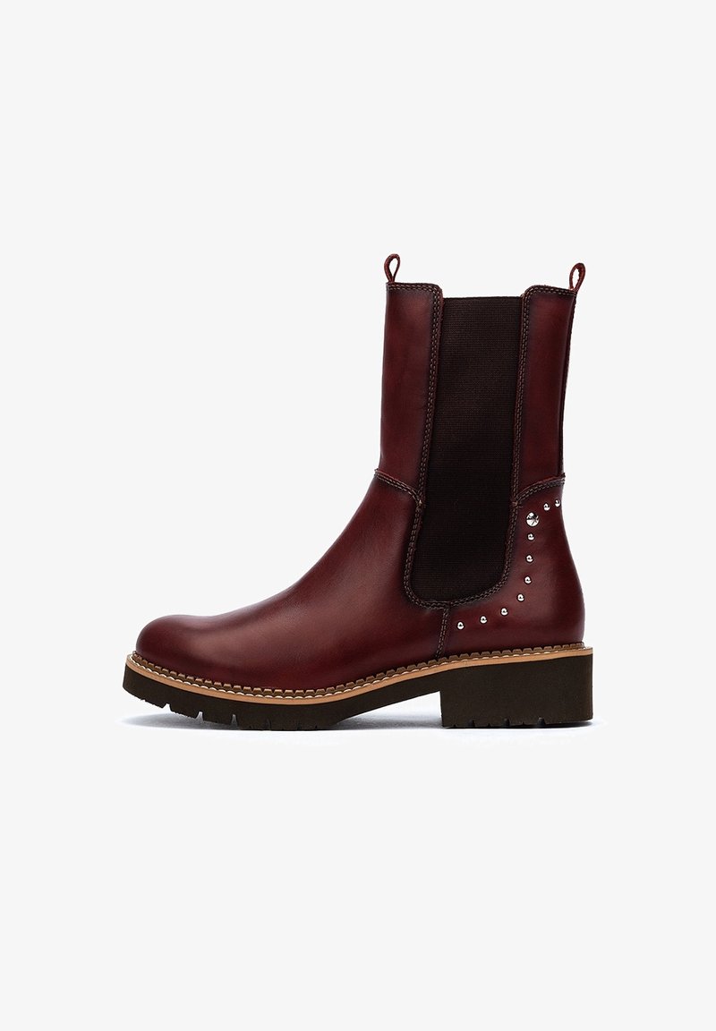 Bottine en cuir rouge foncé avec panneau latéral élastique noir, détails cloutés sur le talon, languettes de traction, semelle brune et semelle noire épaisse.