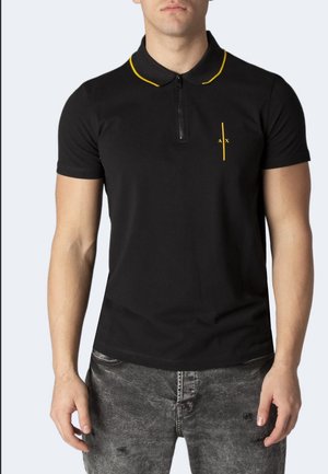 Homme portant un polo noir à manches courtes avec un bord jaune sur le col et une ligne verticale jaune avec "A X" sur la poitrine gauche.